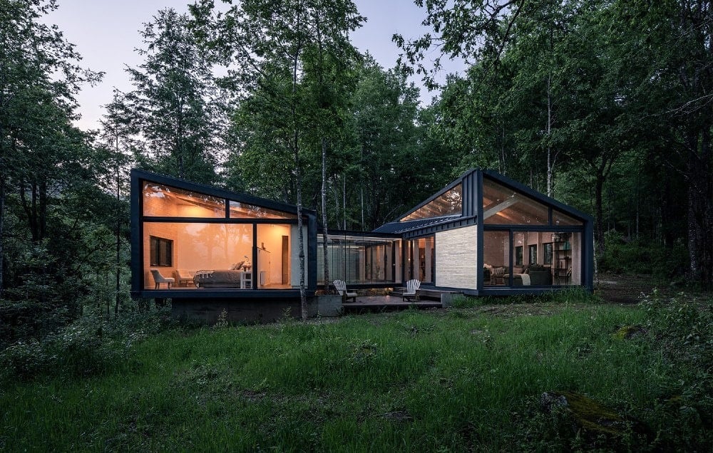 Casa Bosque: volúmenes oscuros vidriados iluminados al atardecer en el bosque