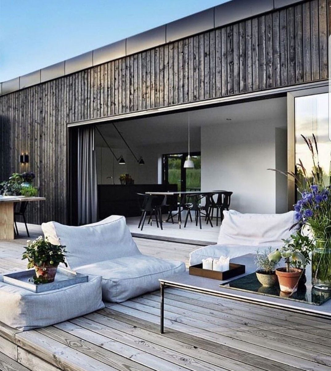 Fachada de madera oscura con grandes aberturas que integran el interior con una terraza de deck