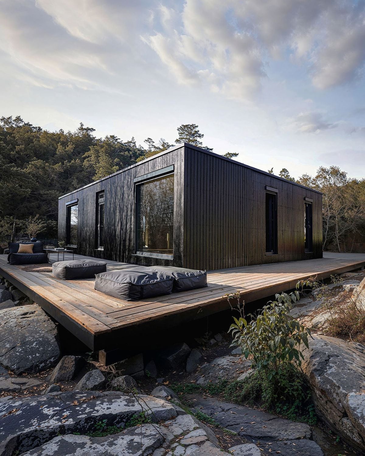 Módulo habitacional de fachada negra con amplio deck de madera, apoyado entre rocas y vegetación