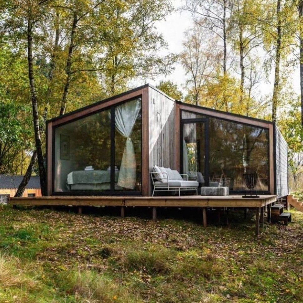 Casa Raíz: módulo de madera con grandes ventanales sobre un deck elevado en el bosque